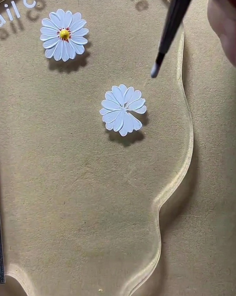 Ein Dotting-Tool platziert einen gelben Punkt in die Mitte des Gänseblümchen-Designs.