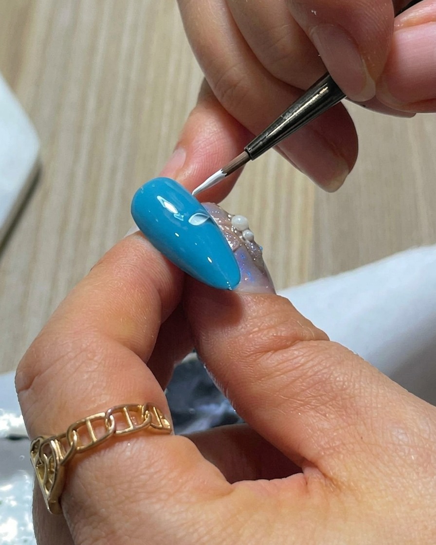 Nahaufnahme eines blauen Nagels mit zwei weißen Gel-Blütenblättern, die mit der Drück-und-Heb-Technik nebeneinander gemalt wurden.