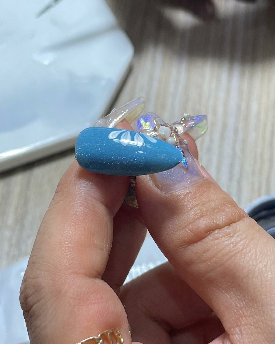 Eine Nahaufnahme des Pinsels einer Nageldesignerin, der auf einer Palette abgewischt wird, um die Menge der weißen Gelpolitur zu kontrollieren.