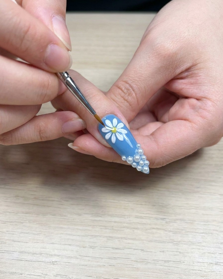 Nahaufnahme eines Pinsels, der weißes Gel auf ein Gänseblümchen-Blütenblatt aufträgt, um die Farbdichte zu verbessern.