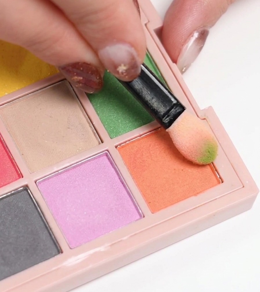 Ein Make-up-Schwämmchen nimmt orangefarbenes Gel von einer Palette auf, um es auf einen Nagel aufzutragen.