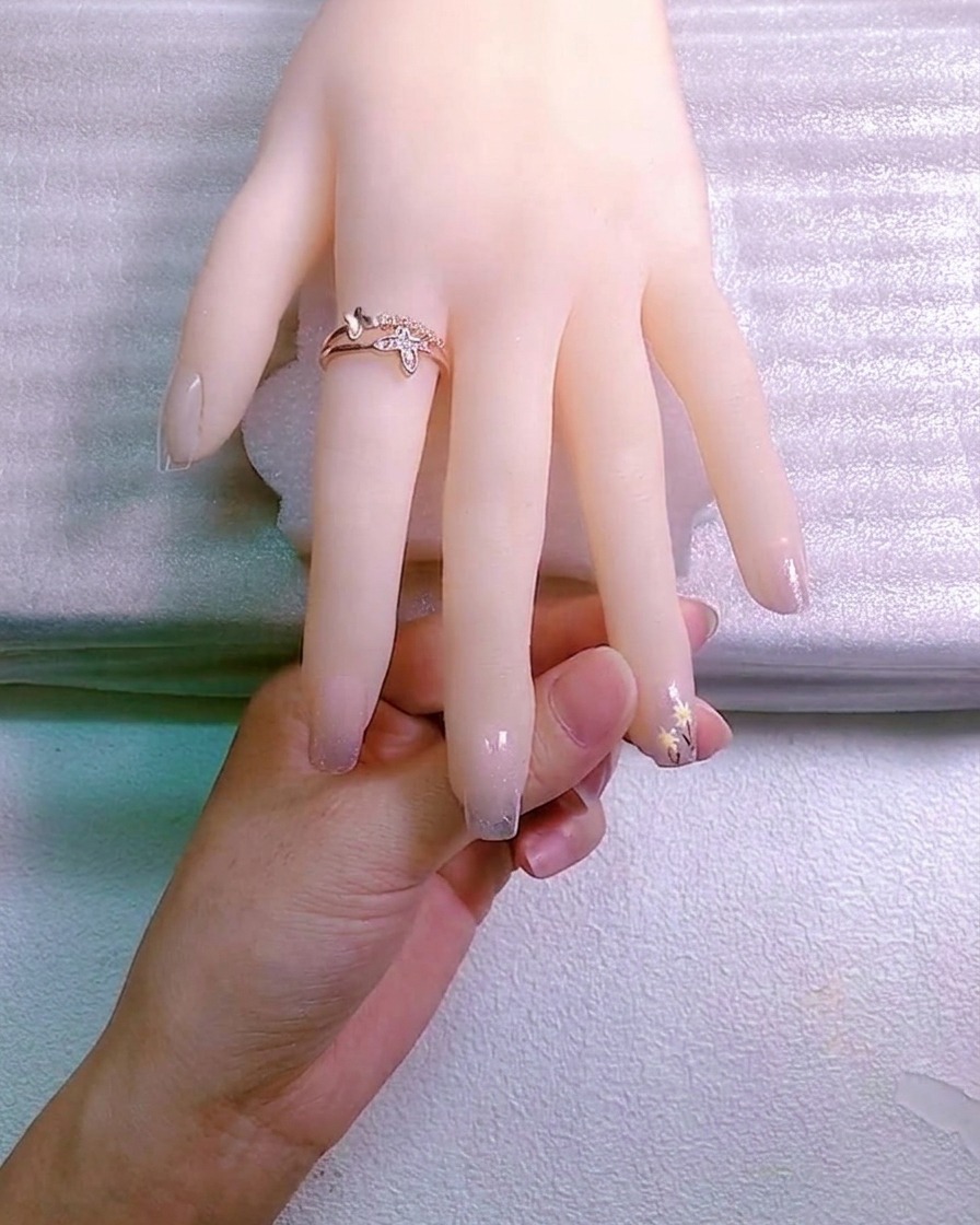 Ein Nail-Art-Werkzeug platziert einen kleinen Kristall-Charm in einem Tropfen Haftgel auf dem Fingernagel.