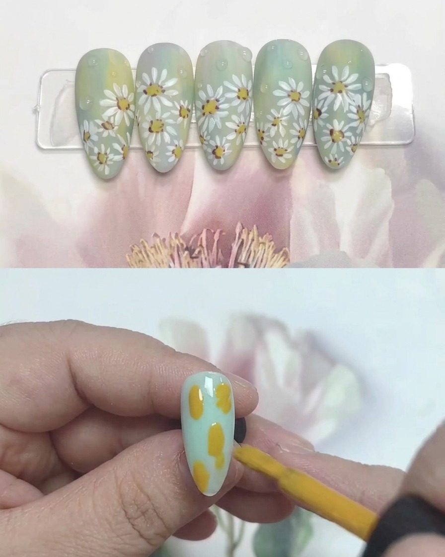 Ein Nagelpinsel beim Auftragen von gelben, blauen und weißen Gelfarbklecksen auf einen klaren Kunstnagel.