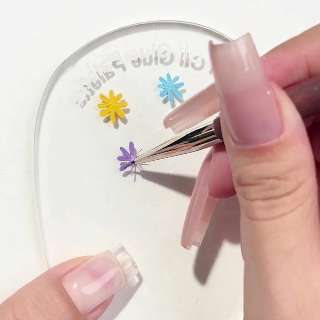Ein Liner-Pinsel trägt ein drittes violettes Blütenblatt auf das Blumendesign auf der Palette auf.