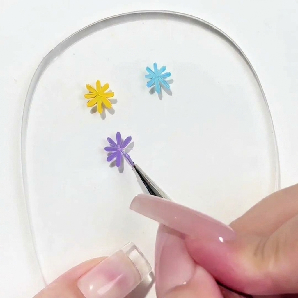 Nahaufnahme eines Detailpinsels, der ein Blütenblatt an eine teilweise fertige violette Blüte auf einer klaren Palette aufträgt.