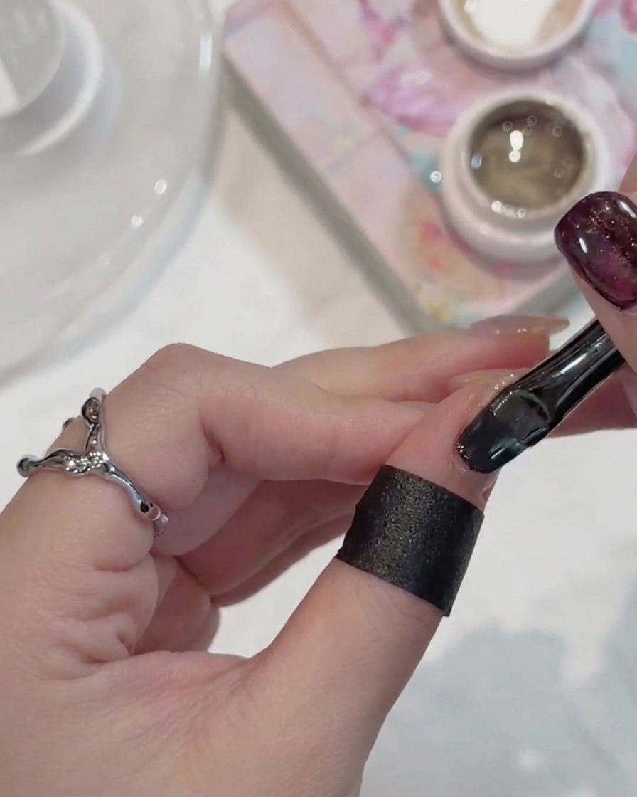 Ein Nagelpinsel trägt dunkles, schimmerndes Cat-Eye-Gel auf einen Fingernagel auf.