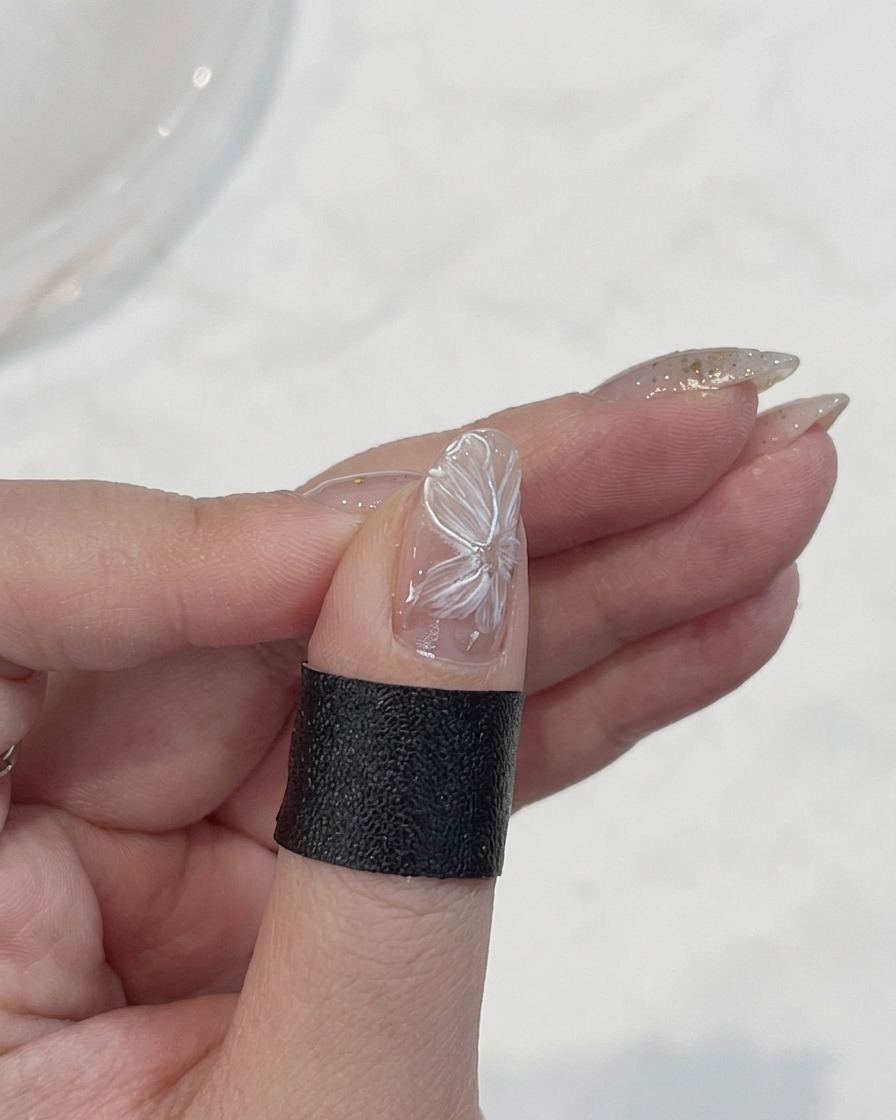 Ein feiner Liner-Pinsel zieht die zarten Ränder der weißen Blütenblätter auf einem Nagel nach.