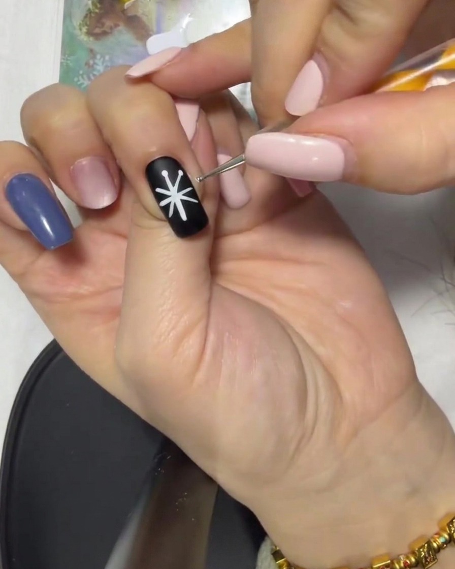 Nahaufnahme eines schwarzen Nagels mit einer weißen Stern-Führung, deren Spitzen mit einem Liner-Pinsel zum Zentrum verbunden werden.