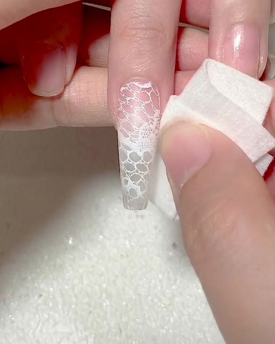 Ein Make-up-Schwamm tupft weißes Gel auf die Nagelspitze für einen Ombré-Effekt.