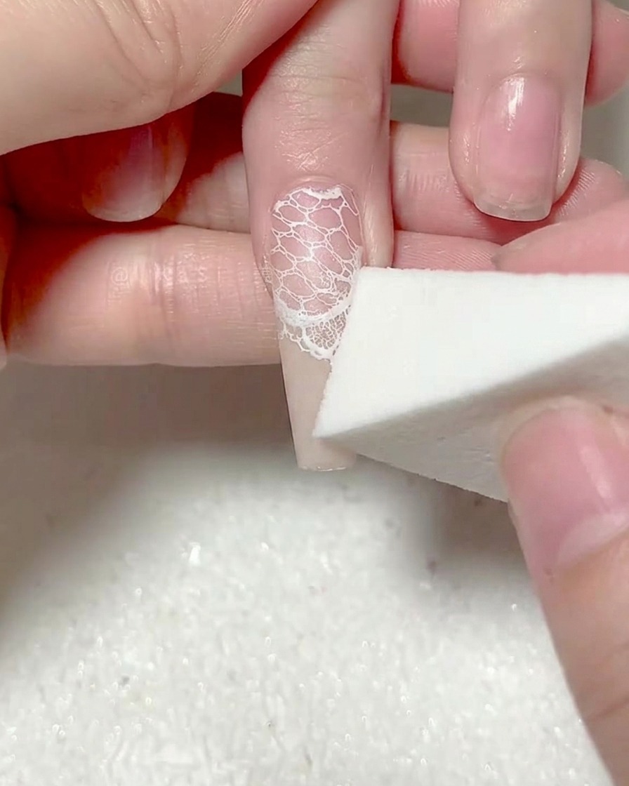 Ein Make-up-Schwamm patzt eine zweite Schicht weißes Gel auf die Nagelspitze.