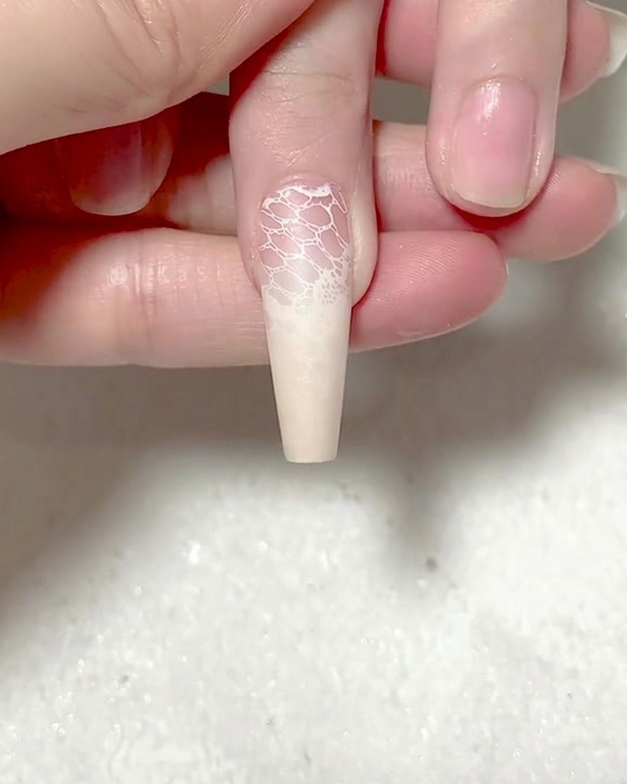 Eine Pinzette platziert einen roten Rosen-Sticker auf der Nagelmitte.