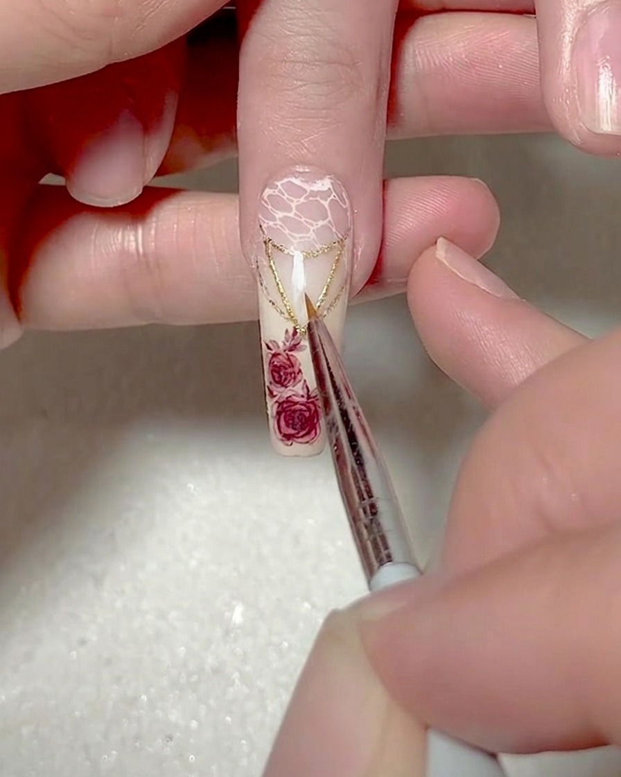 Ein feiner Liner-Pinsel malt ein weißes Dreieck auf die Nagelspitze.
