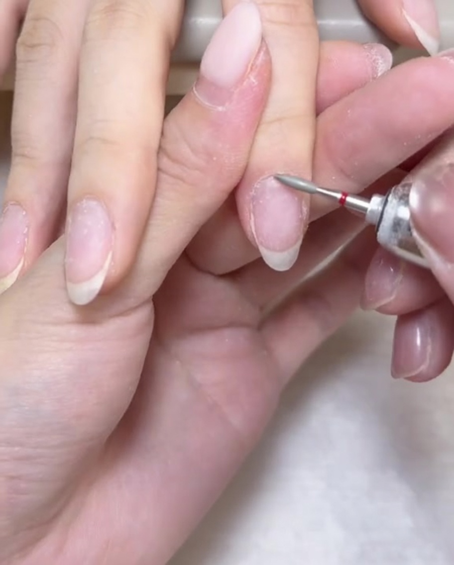 Ein e-File Fräser wird verwendet, um den Nagelhautbereich um die Nagelbasis vorsichtig zu reinigen und zu öffnen.