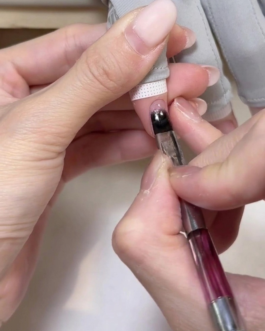 Eine Hand befindet sich in einer tragbaren UV-Lampe, während die Nägel zur Aushärtung des Basis-Gels beleuchtet werden.