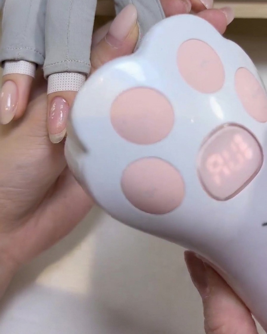 Eine kleine, katzenpfotenförmige Hand-UV/LED-Lampe wird über einen Fingernagel gehalten, um das Gel zu härten.