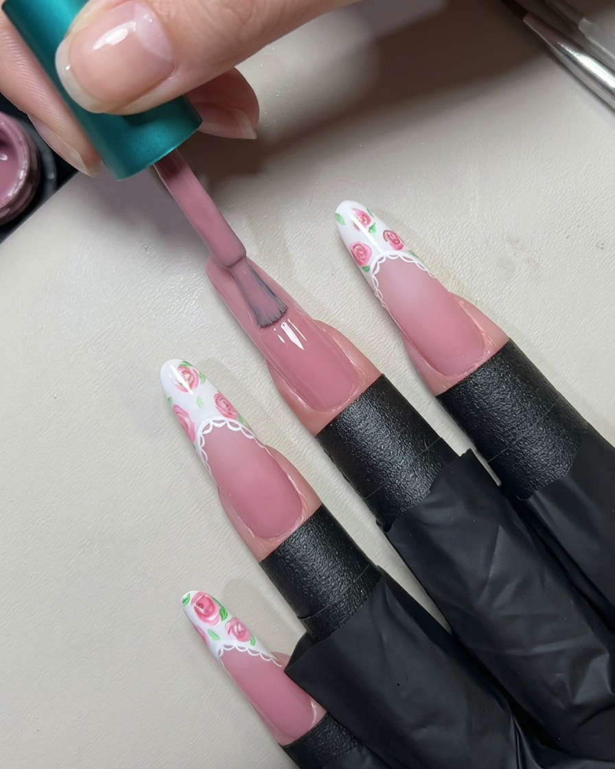 Ein Nagellackpinsel trägt eine Schicht durchscheinendes, nudefarbenes Pink-Gel auf einen langen, vorbereiteten Fingernagel auf.