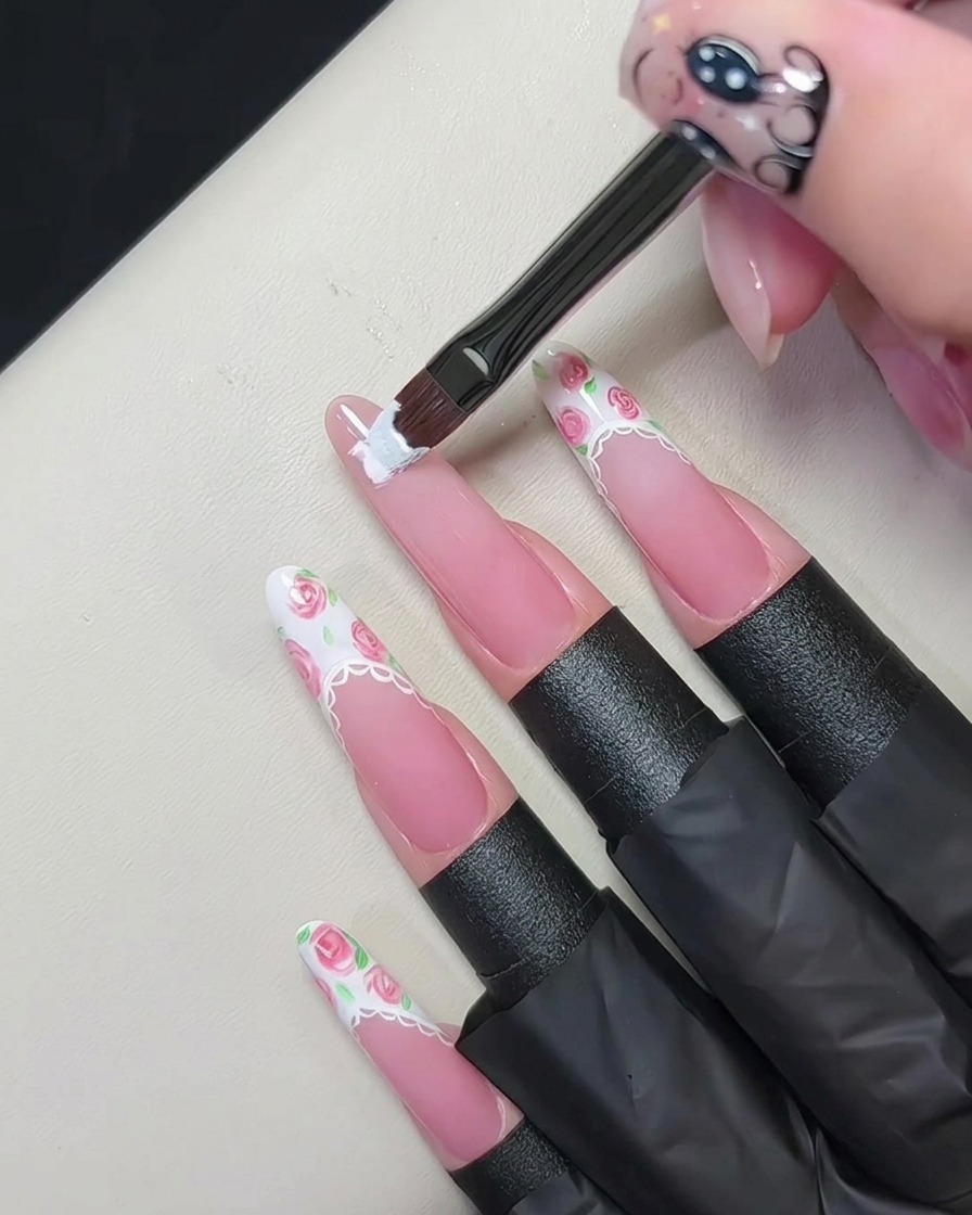 Ein flacher Gelpinsel malt eine dicke weiße French-Spitze auf den Rand eines nudefarbenen Fingernagels.