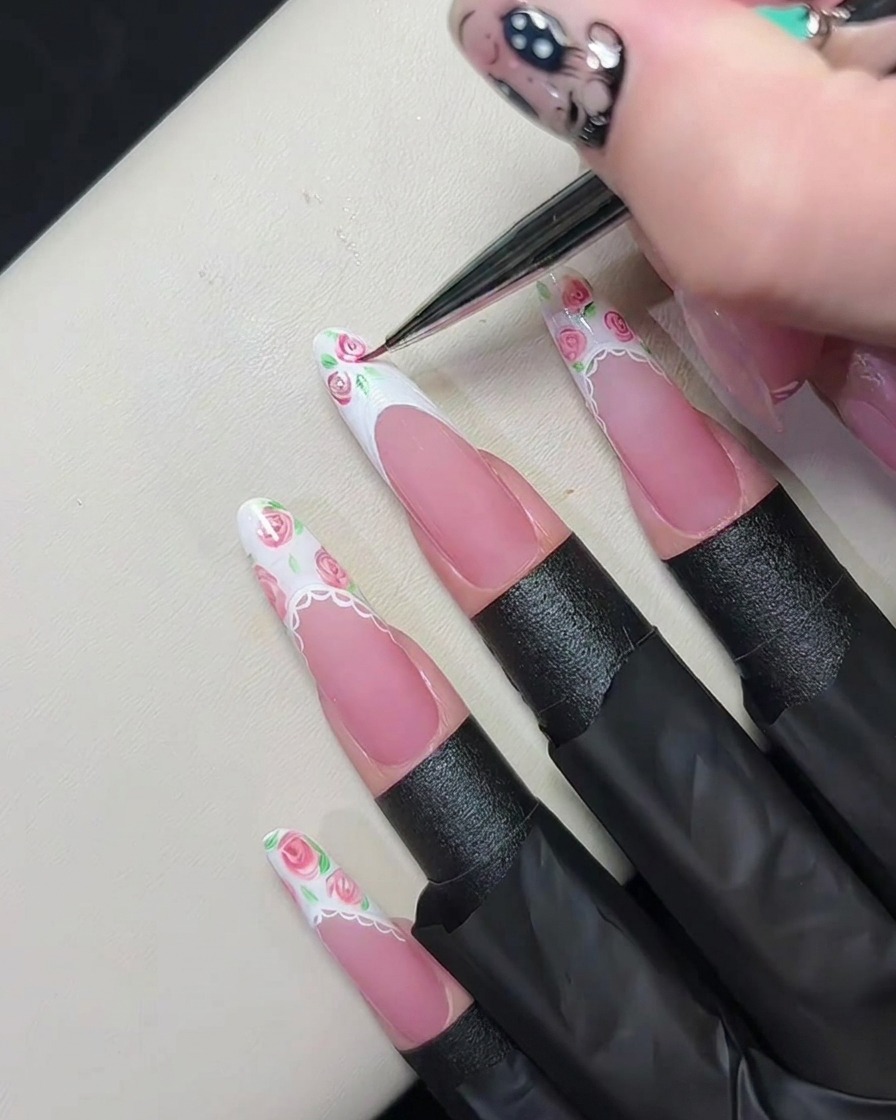 Ein feiner Liner-Pinsel verwirbelt pinkes Gel im nassen weißen Gel auf einer French-Spitze, um winzige Rosenmuster zu erzeugen.