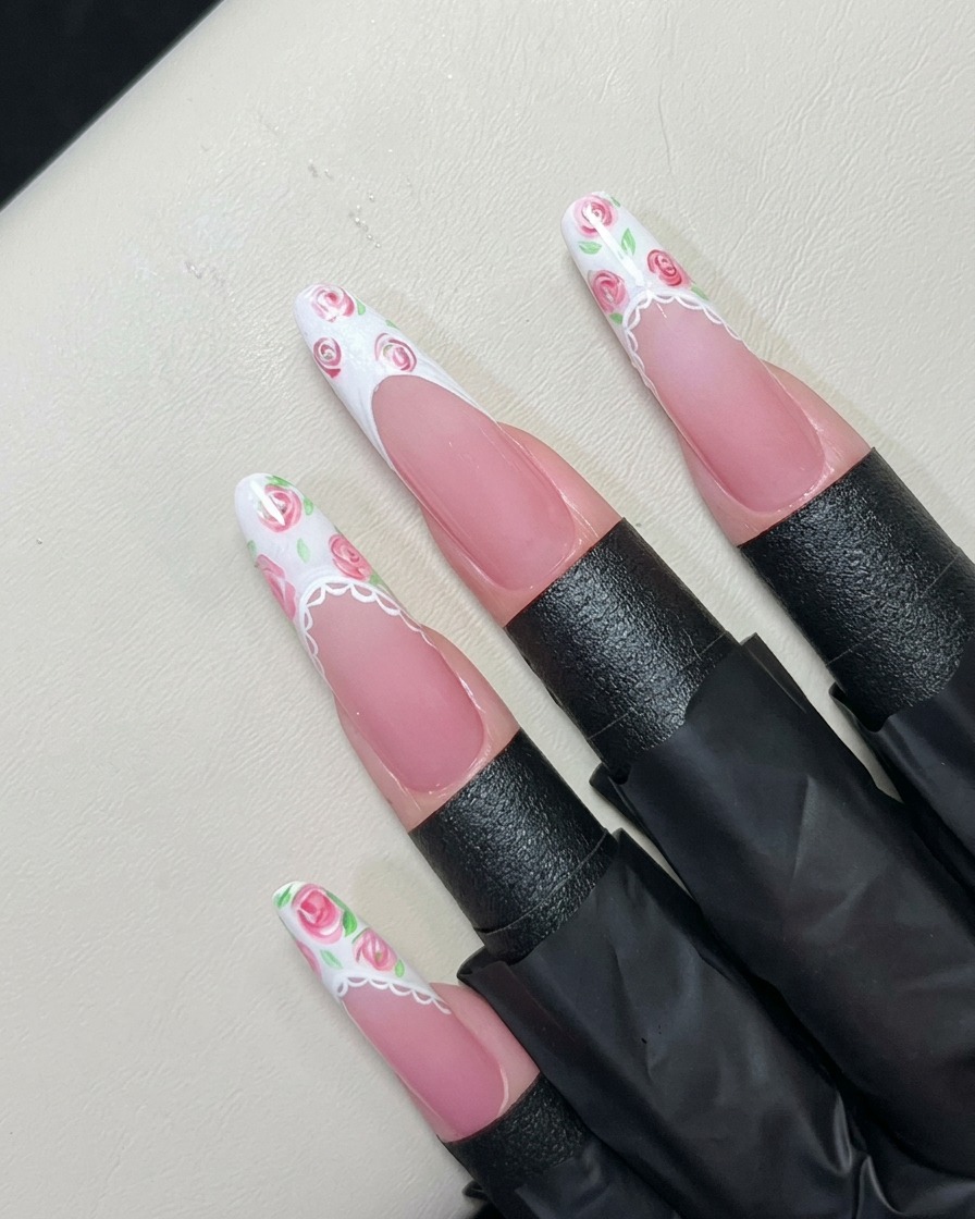 Ein feiner Liner-Pinsel malt winzige grüne Blätter um die pinken Rosen auf einer weißen French-Spitze.
