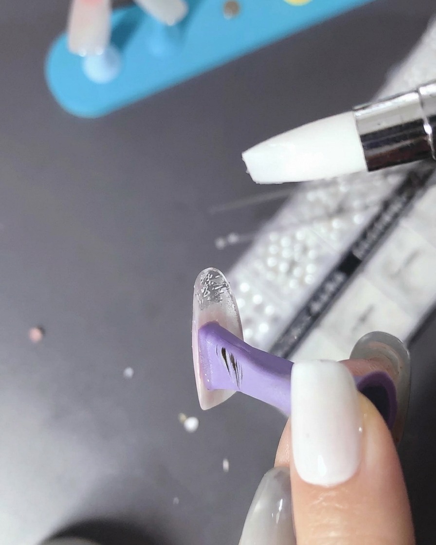 Ein Pinsel trägt einen kleinen Tropfen klares Bead-Gel auf die ausgehärtete Nageloberfläche auf.