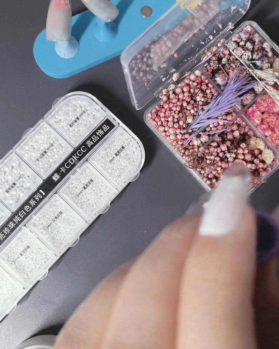 Eine Pinzette platziert ein kleines Trockenblumenblatt auf dem feuchten Gel des Nagels.