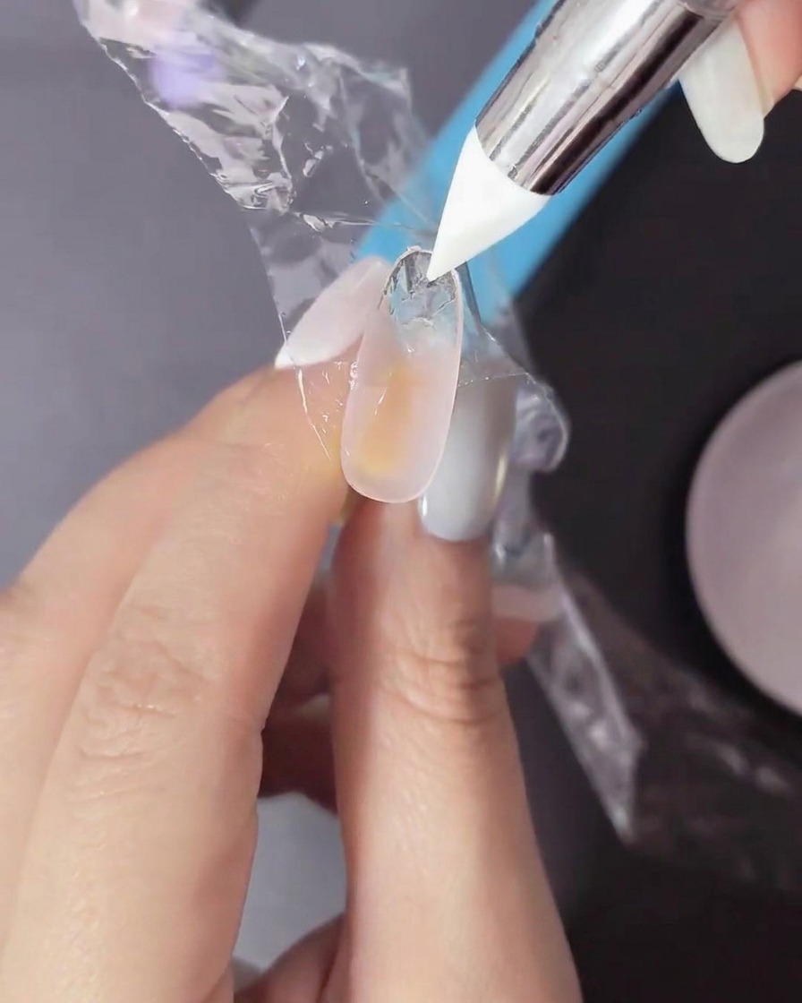 Ein Finger mit nicht ausgehärtetem Gel wird mit einer dünnen Plastikfolie und einem Silikonwerkzeug bearbeitet, um eine Textur zu erzeugen.