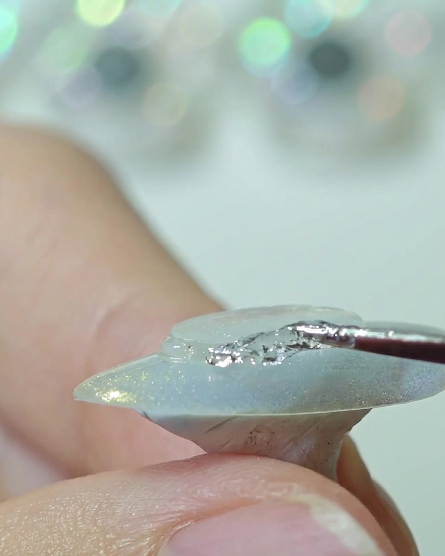 Ein Silikon-Tool drückt eine Kunststoffscheibe auf die Mitte eines Nagels und glättet die Kanten.