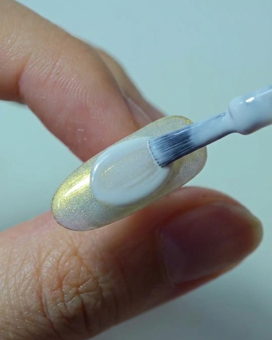 Ein Pinsel trägt eine glatte, deckende zweite Schicht weißes Gel auf den Nagel auf.