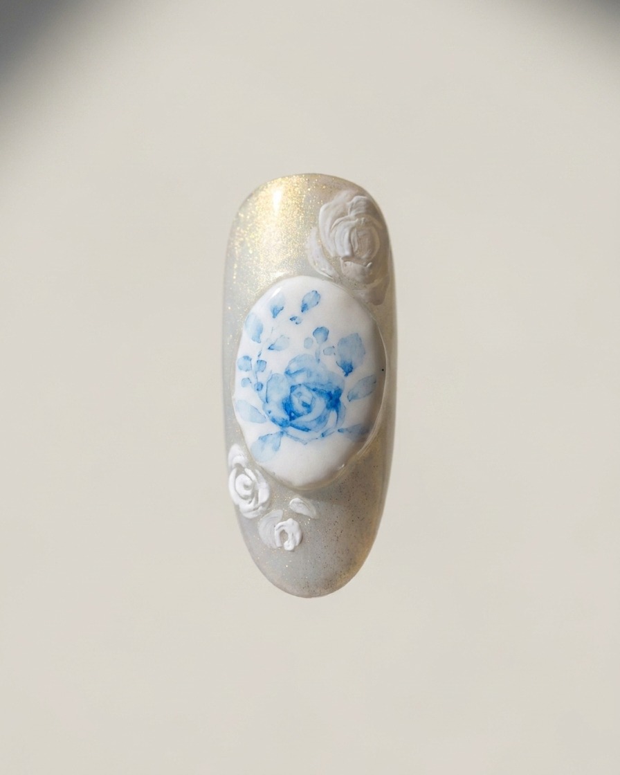 Ein feiner Liner-Pinsel malt weiße Rosenumrisse an den Nagelrändern um das zentrale blaue Rosendesign.