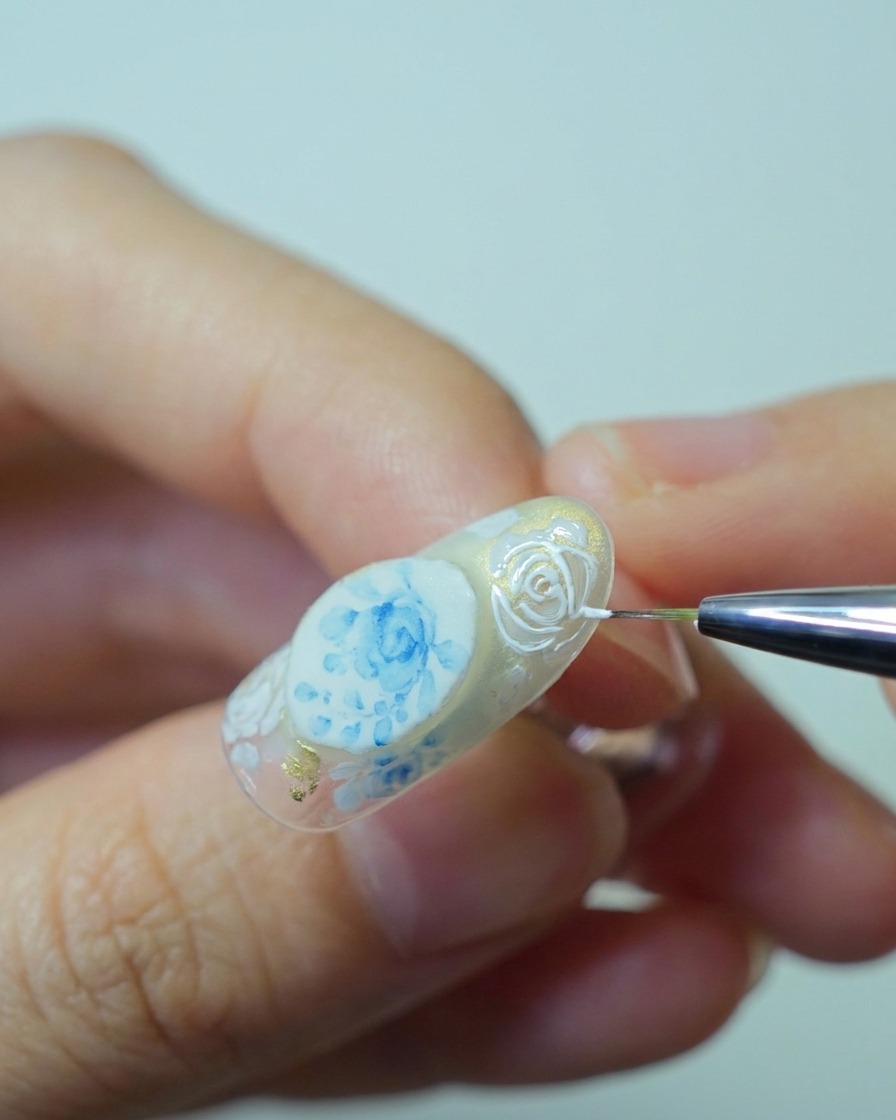 Nahaufnahme eines Pinsels, der dickes weißes Relief-Gel auf die Rosenumrisse aufträgt, um 3D-Textur aufzubauen.