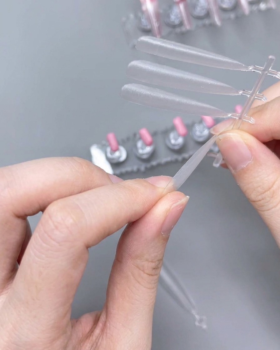 Eine Nahaufnahme von Händen, die eine Handfeile verwenden, um den Rand eines klaren künstlichen Nagels zu formen.