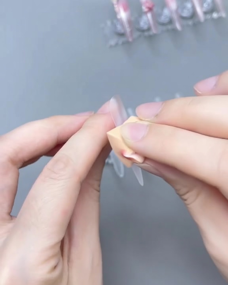 Ein Pinsel verblendet das zartrosa Gel auf dem Nageltipp, um einen Ombré-Farbverlauf zu erzeugen.