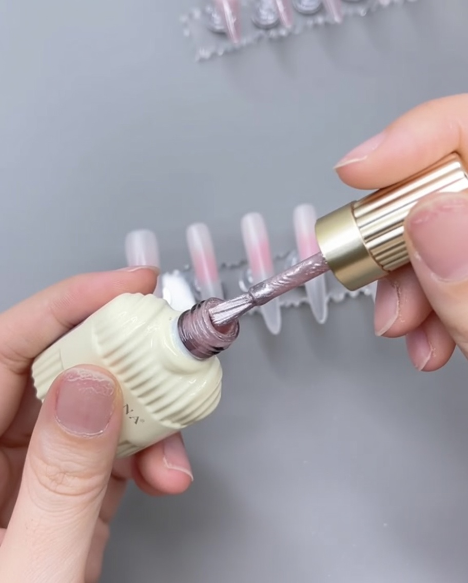Ein Nagelpinsel trägt rosa Cat-Eye-Gel über einer ausgehärteten, zartrosa Basis auf einem Nageltipp auf.