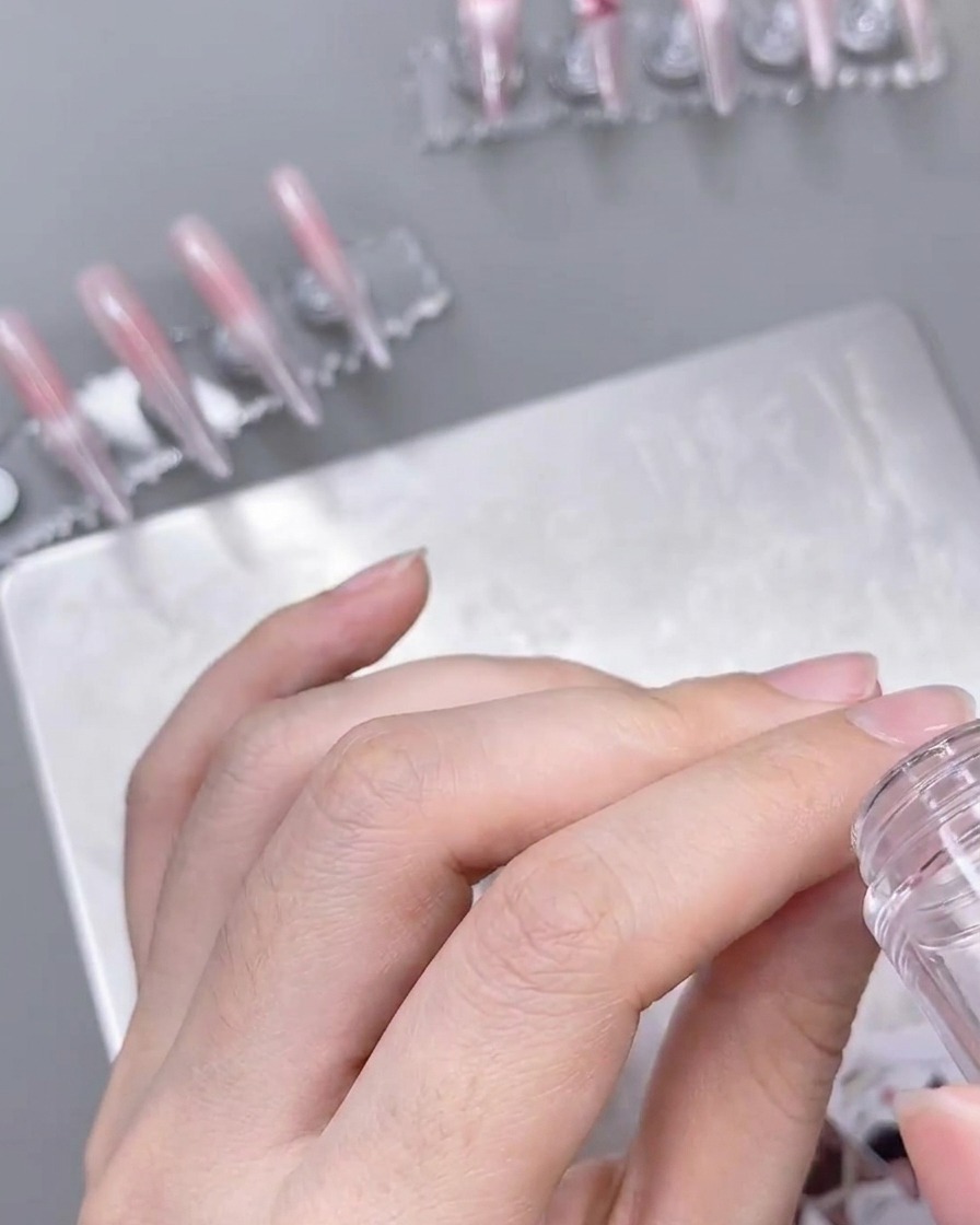 Ein klarer Stempel trägt ein feines weißes Spitzenmuster auf einen vorbereiteten, ombré-farbenen Nagel auf.
