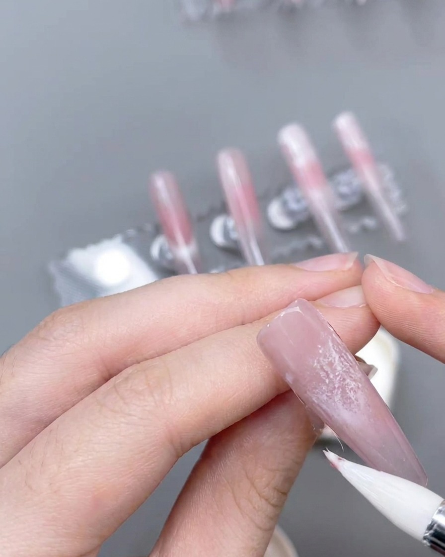 Ein feiner Liner-Pinsel kreiert dünne, präzise rosa Akzentlinien auf einem verzierten Nagel.