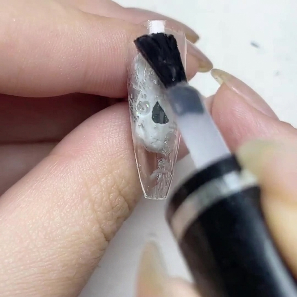 Ein Pinsel trägt matten Überlack auf den mit Silberfolie verzierten Nagel auf.
