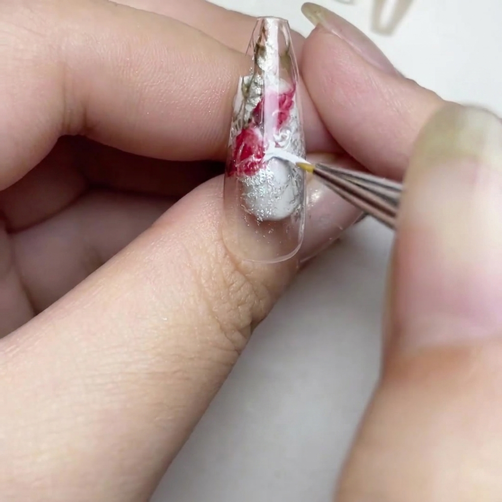 Nahaufnahme eines Nagels, auf dem ein Pinsel weiße Striche für einen weichen Aquarell-Effekt in den klaren Bereichen hinzufügt.