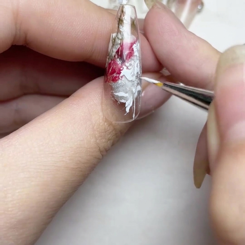 Nahaufnahme des Nagels mit verfeinerten weißen Linien und einer kleinen, detaillierten weißen Blütenknospe an der Spitze.