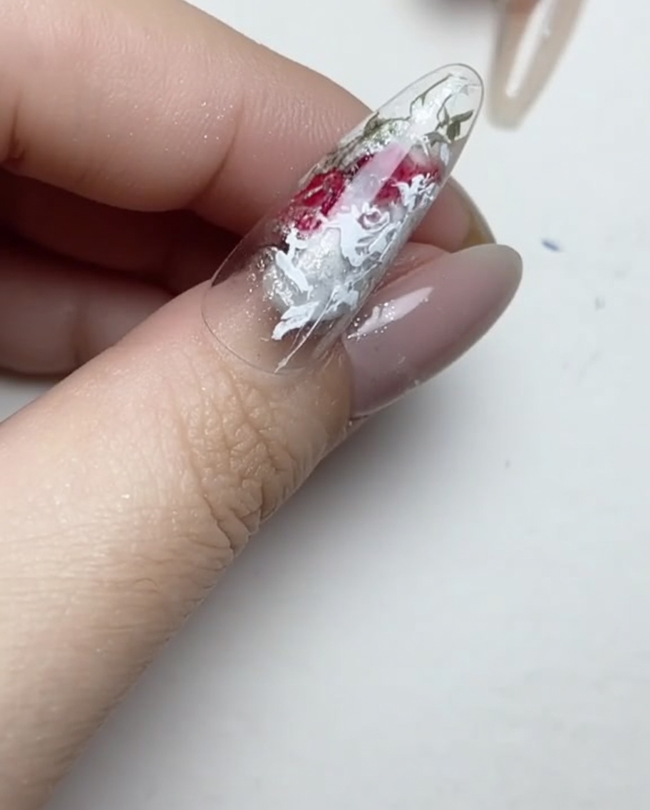 Ein Liner-Pinsel beim Auftragen kleiner, klarer Punkte Gel-Kleber auf die Oberfläche eines manikürten Nagels.