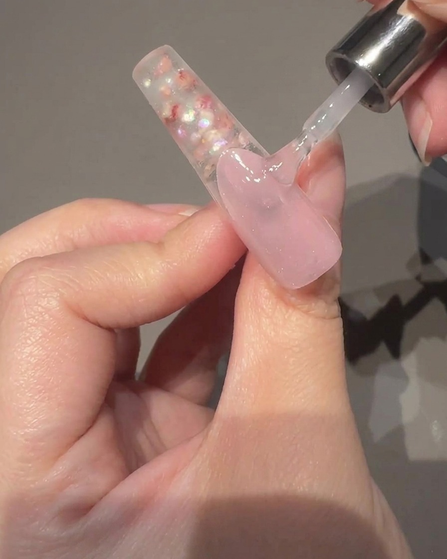 Nahaufnahme einer Hand, die einen Magnetstab neben einen mit nassem Cat-Eye-Gel beschichteten Nagel hält, während der Schimmer in die Mitte wandert.