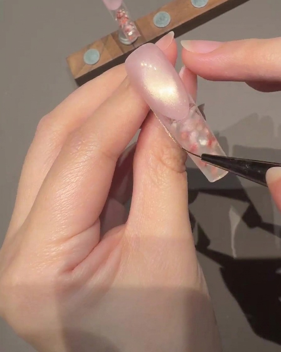 Ein Pinsel trägt einen klaren, glänzenden Top Coat auf die Oberfläche des verzierten Nagels auf.