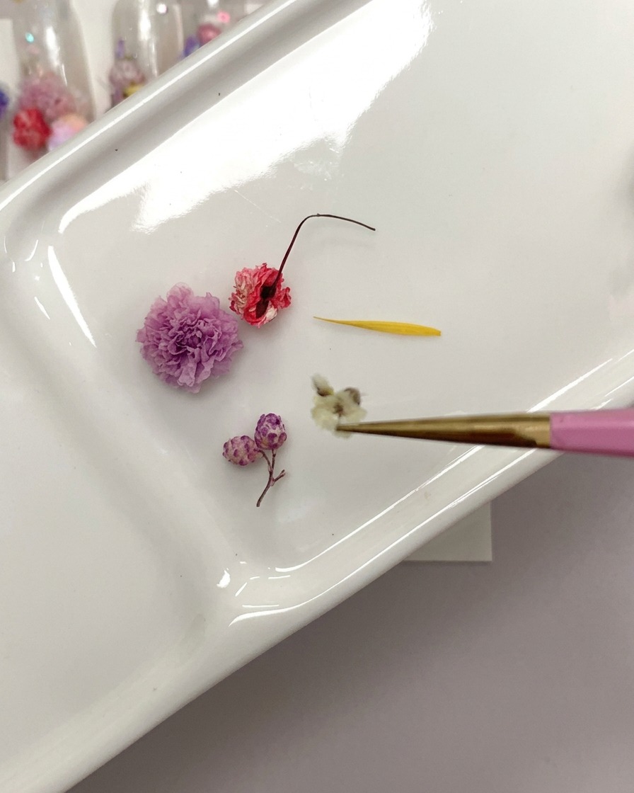 Nahaufnahme einer Pinzette, die eine getrocknete Rose hält, während der Stielansatz gekürzt wird.
