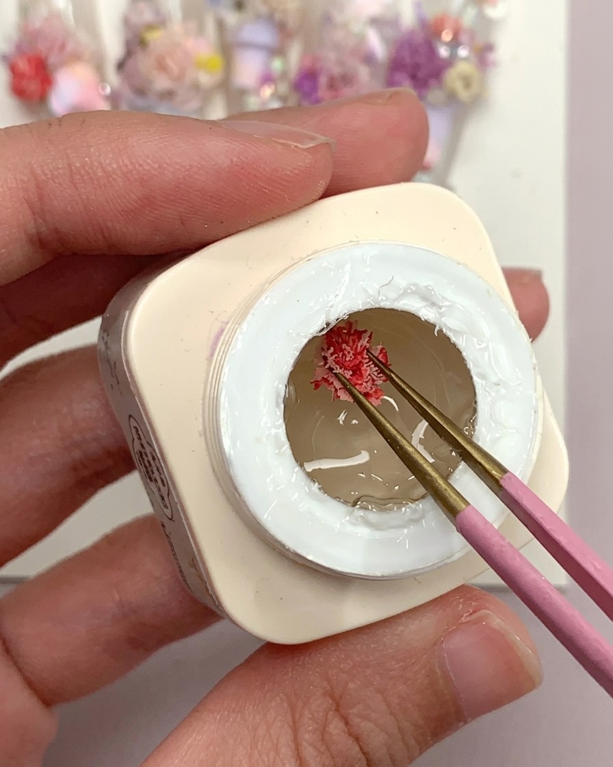 Ein Pinsel trägt einen Tropfen durchsichtiges Frosted-Gel auf eine klare Kunststoff-Nagelspitze auf.