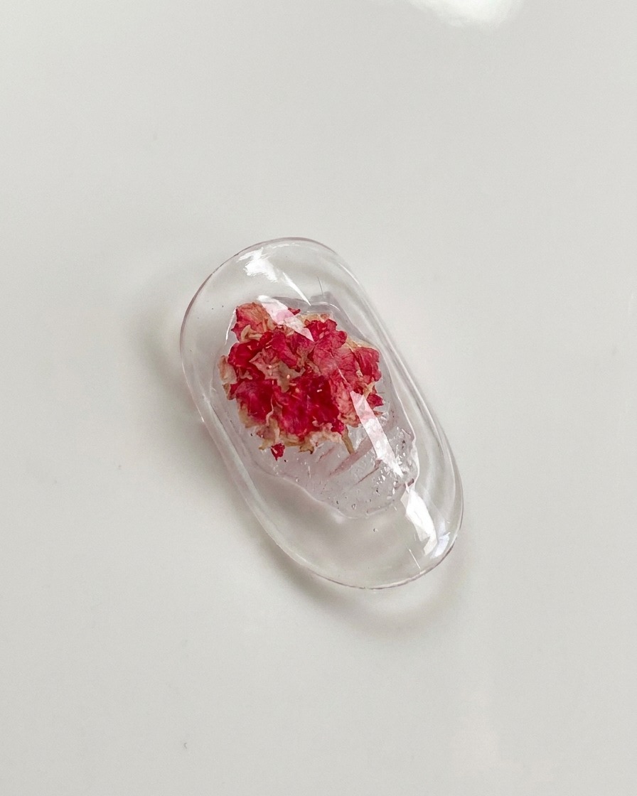 Ein Detailpinsel drückt vorsichtig auf die Blütenblätter einer im Nagelgel eingebetteten Trockenrose.
