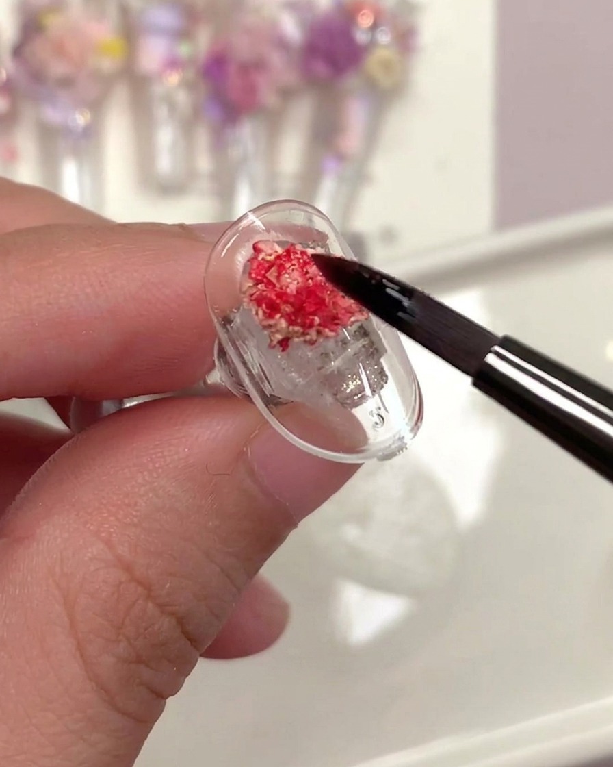 Ein Pinsel trägt einen durchsichtigen Top-Coat über eine Trockenrose auf einem Nagel auf.