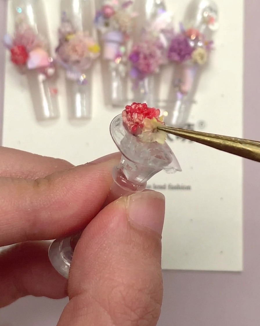 Eine Pinzette hält ein kleines florales Nagelornament, nachdem es versiegelt wurde.