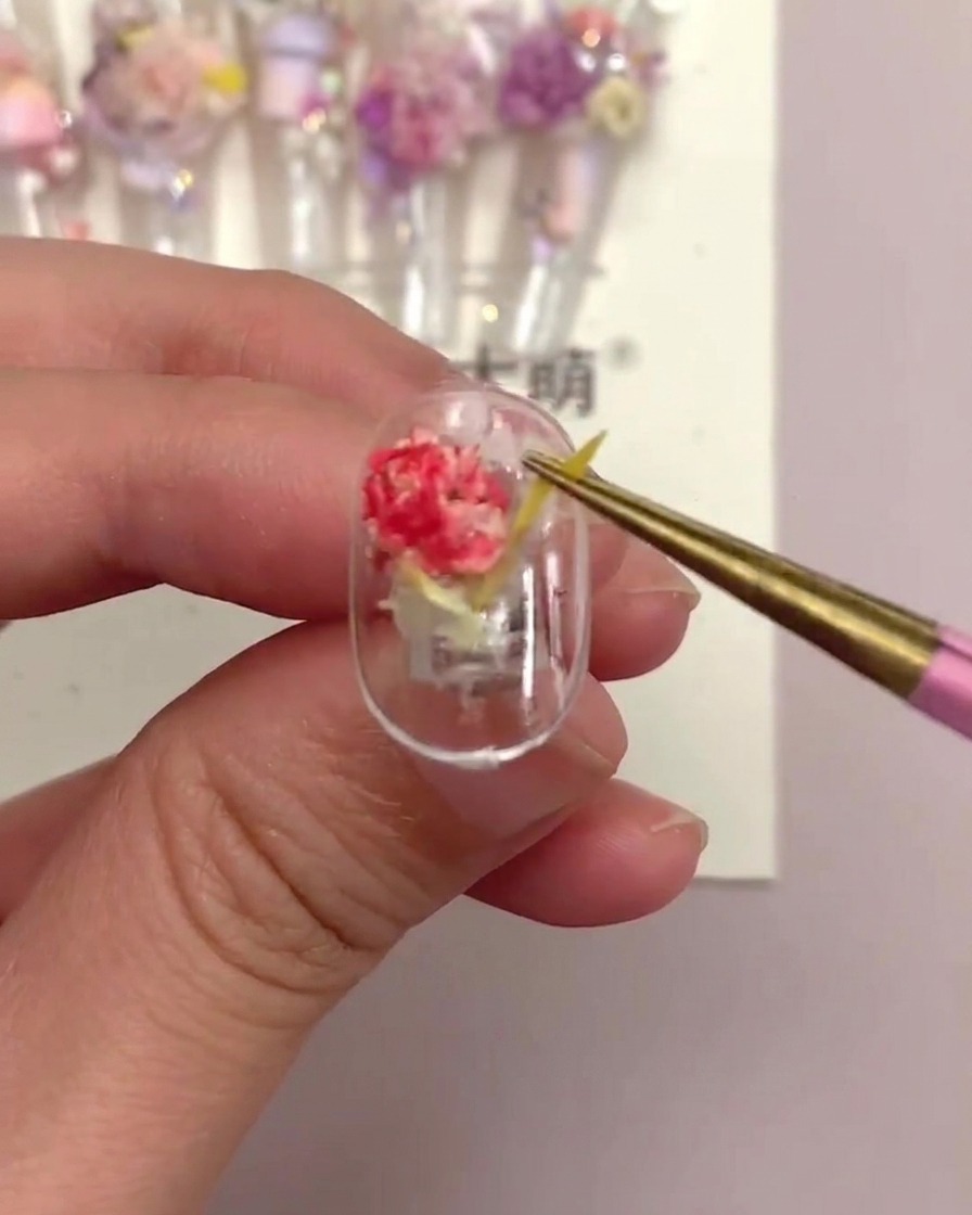 Eine Pinzette zieht vorsichtig an einem gelben, linearen Blumenstück auf einer fertigen Nagelspitze, um den Halt zu testen.