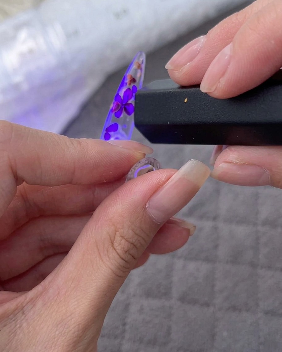 Hand hält eine tragbare UV/LED-Lampe über einen verzierten Nageltip.