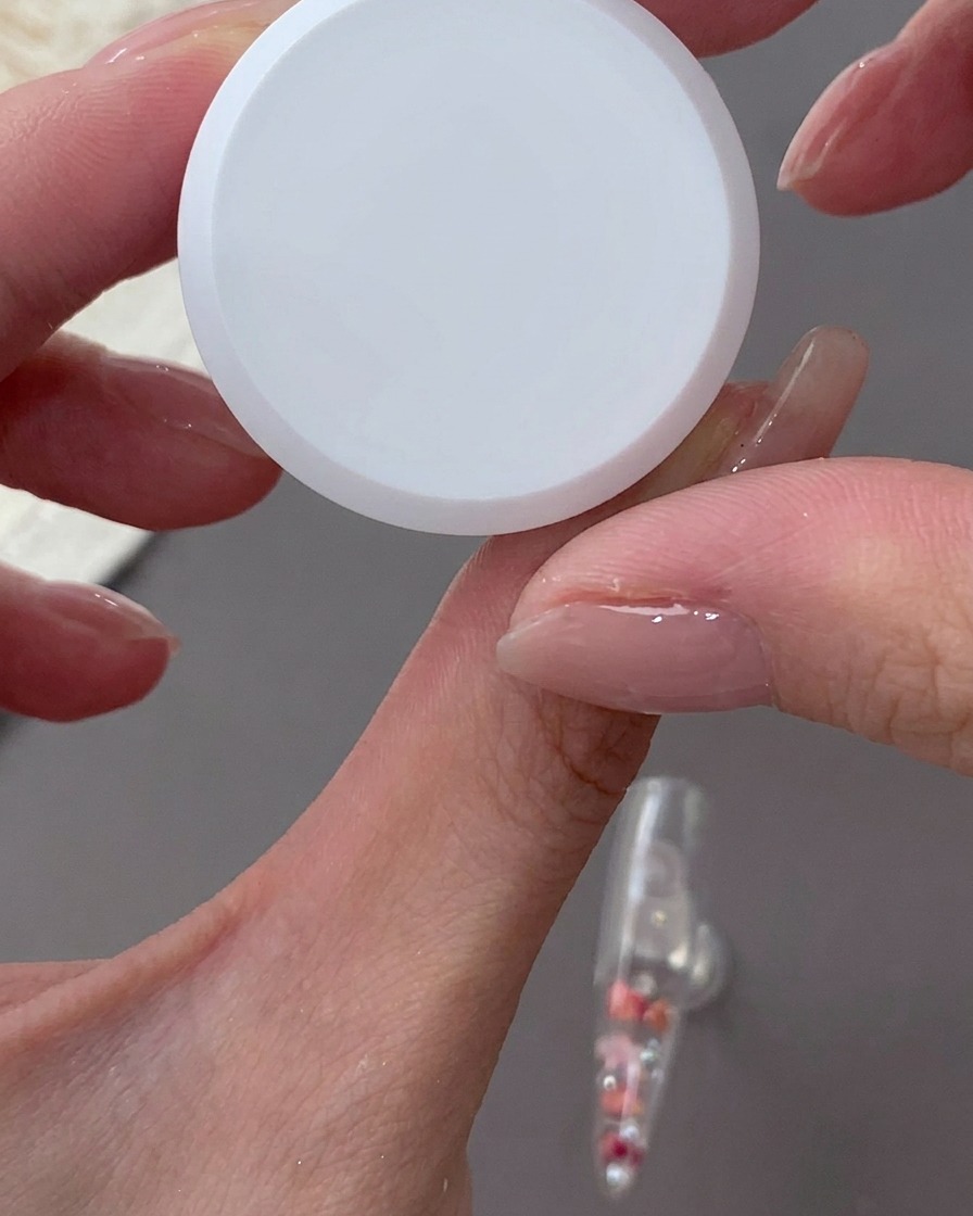 Ein Schwamm tupft milchig-weißes Gel auf den hinteren Bereich eines klaren Nageltips.