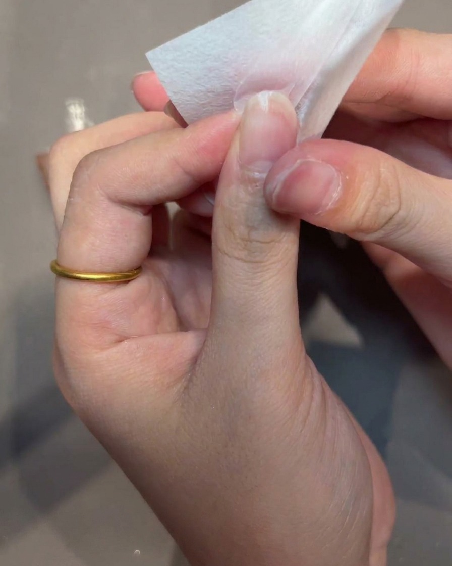 Nahaufnahme einer Hand, die mit einer fusselfreien Zellette die Oberfläche eines Nageltipps reinigt.
